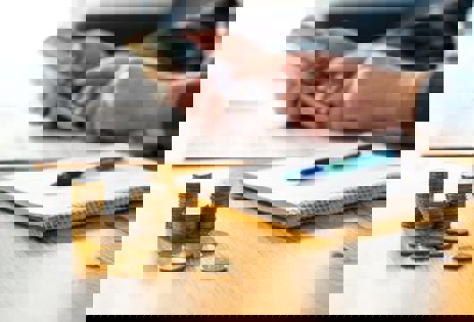 Desk With Money, Pen And Notepad, And Person Using Calculator