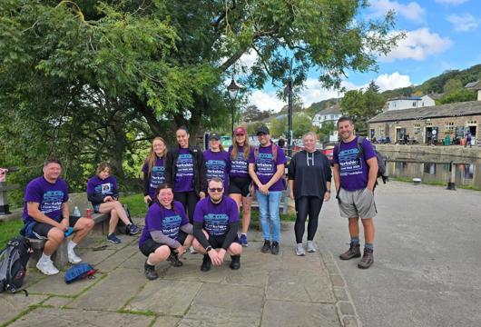 A group of colleagues wearing purple Candlelighters charity walk T-shirts smile for a photo beside a canal in Yorkshire during their 50km fundraising walk.