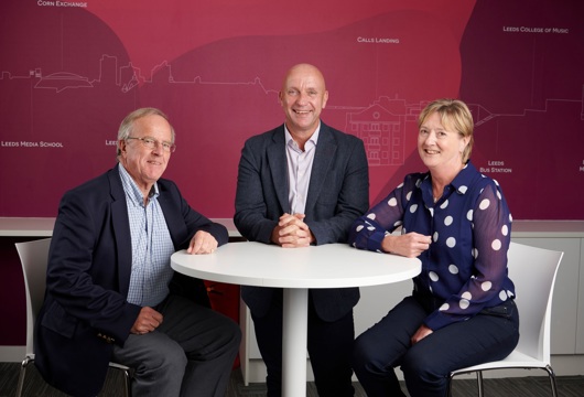 Two men and a woman sitting at a table in an office dressed in business attire