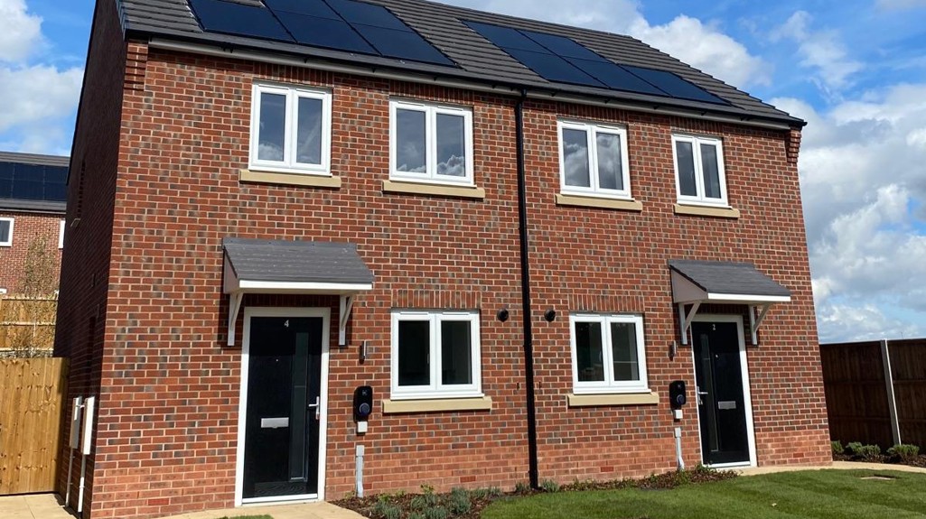 A pair of modern semi-detached houses with black front doors, white-framed windows, solar panels, and neatly maintained front gardens.
