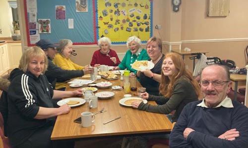 Group of people sitting round a table smiling and holding plates of pancakes