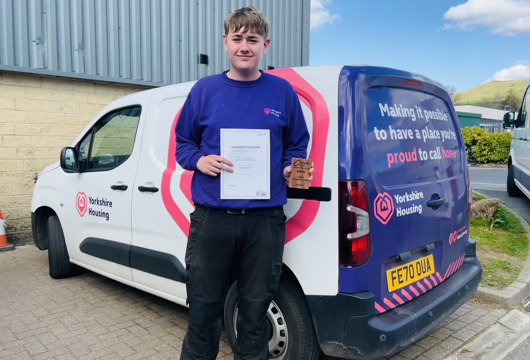 Our award winning apprentice Leon standing with his certificate in front of a Yorkshire Housing van