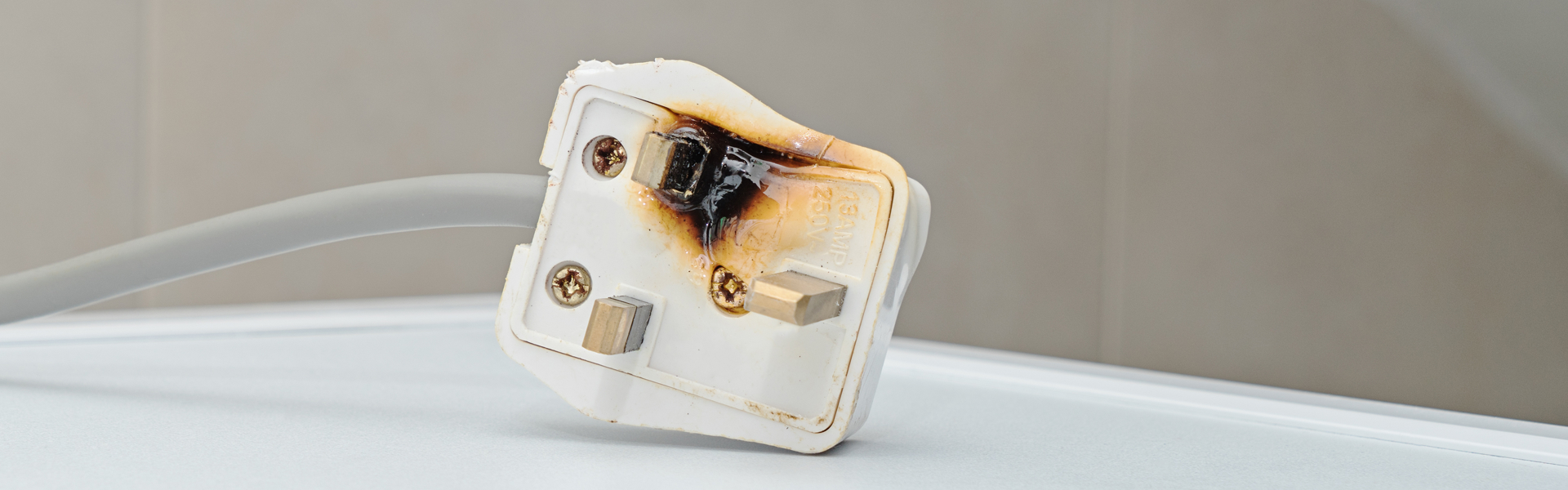 Plug that has been melted and burnt on one side lying on a white surface.