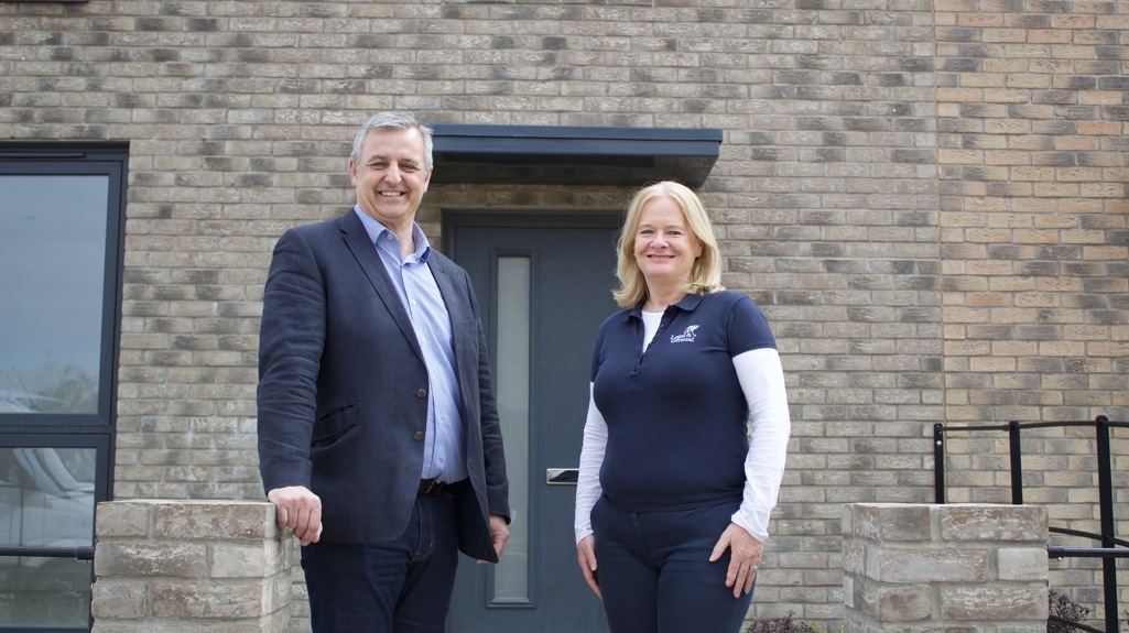 Man and woman stood together smiling in front of a new house. The man is from Yorkshire Housing and the woman is from Legal & General Modular Homes. 