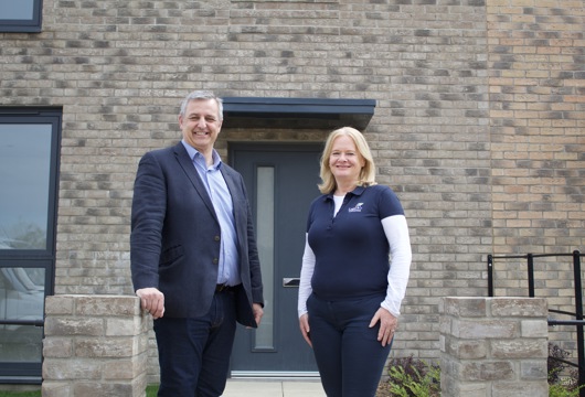 Man and woman stood together smiling in front of a new house. The man is from Yorkshire Housing and the woman is from Legal & General Modular Homes. 