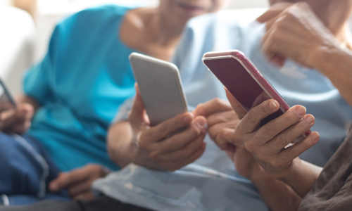 Three people sat on a sofa holding phones, helping each other use them. 