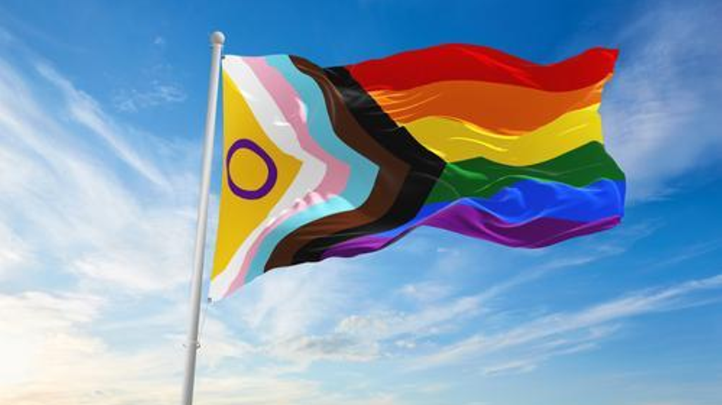 The Pride flag waving against a bright blue sky, its rainbow colours vibrant in the sunlight.