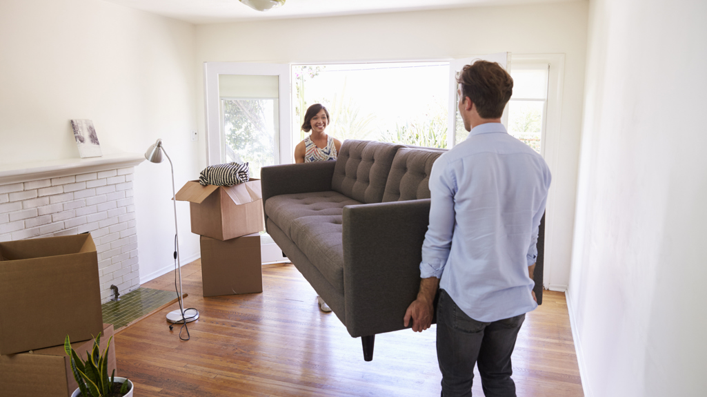 Man and woman carrying a sofa in a living room