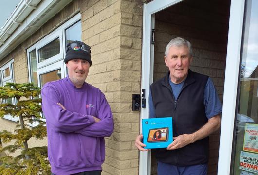 Man standing at his front door holding smart home technology hub box, with another man dressed in Yorkshire Housing work clothes