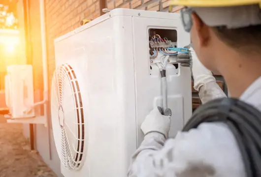 Man checking airforce heat pump wires on the outside of a house with bright sun on the left hand side. 