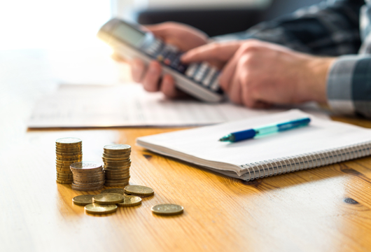 Man using a calculator at a table with a notepad and pen and a pile of coins