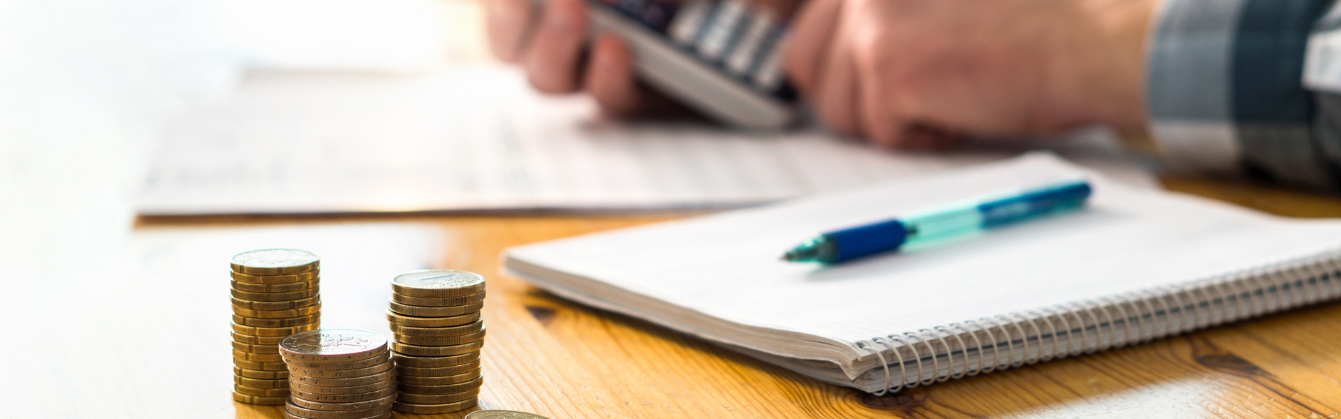Man using a calculator at a table with a notepad and pen and a pile of coins
