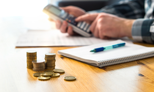 Man using a calculator at a table with a notepad and pen and a pile of coins