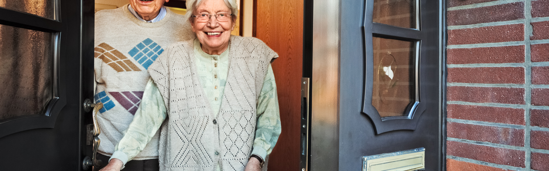 An elderly man and woman cheerily answering the door