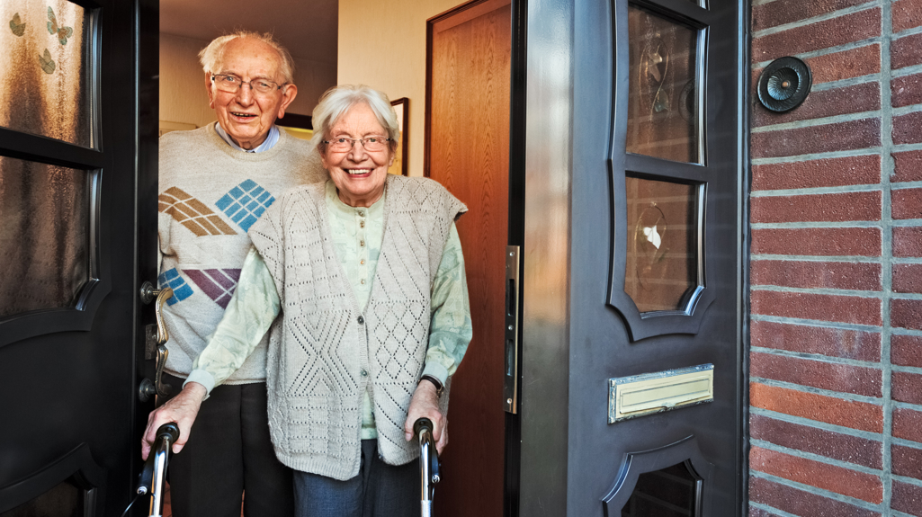 An elderly man and woman cheerily answering the door