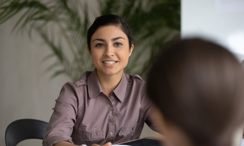 Woman sitting across desk from customer with sheet of paper giving advice 