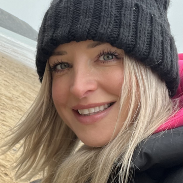 Sarah on a beach wearing a woolly hat and smiling 
