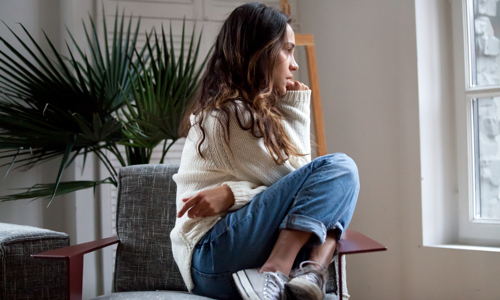 Young woman perched on a chair looking thoughtfully out of the window