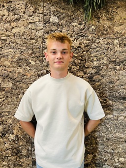 Photo of Lucas leaning against a cork wall smiling