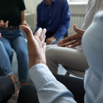Abstract picture of people sat in a circle with one person gesturing using their hands
