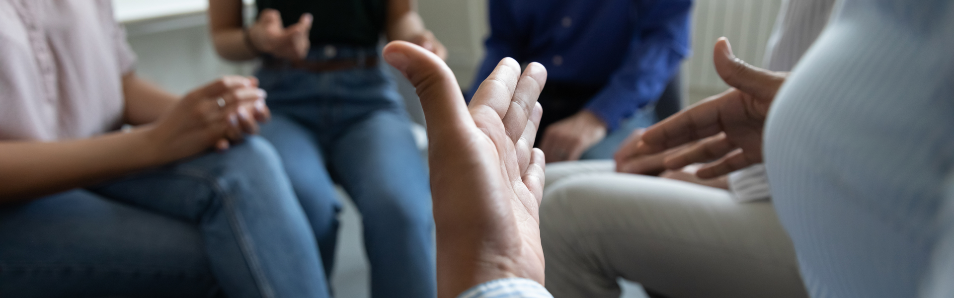 Abstract picture of people sat in a circle with one person gesturing with their hands