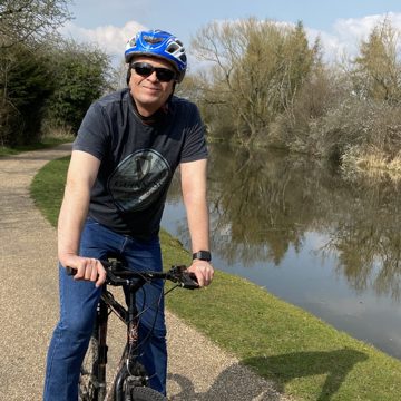 Man on bicycle wearing sunglasses and helmet smiling at camera