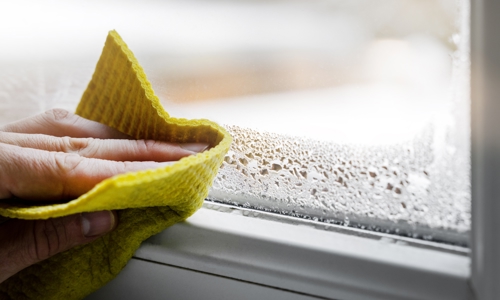 Hand wiping condensation from a window with a yellow cloth on a cold day.