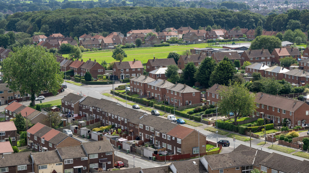An aerial shot of Swarcliffe, you can see lots of terraced houses and a big tree over to the left with a big green field space with a play park towards the back of the photo. 