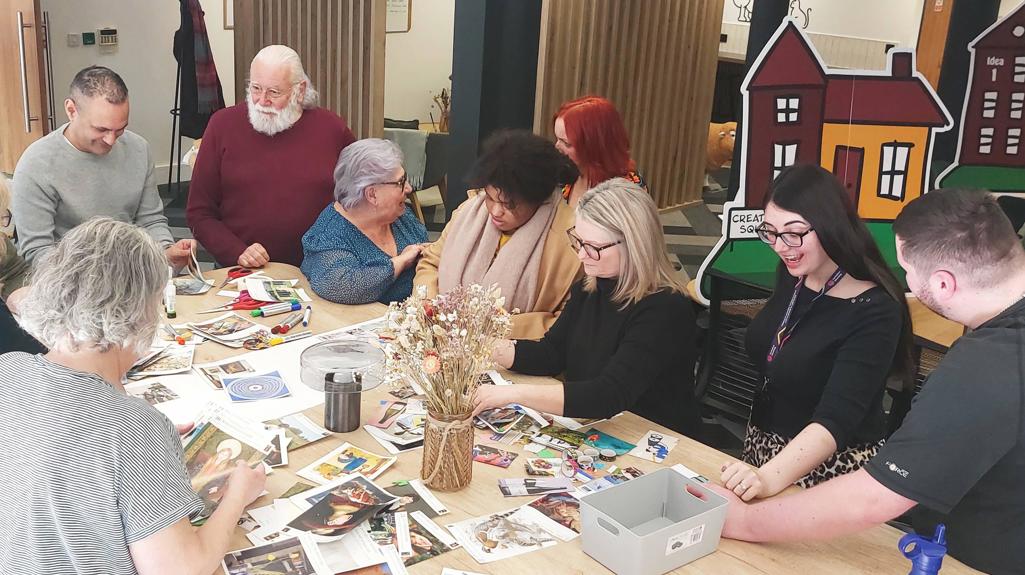 Photo is of a group of customers and colleagues playing game of homes around a table
