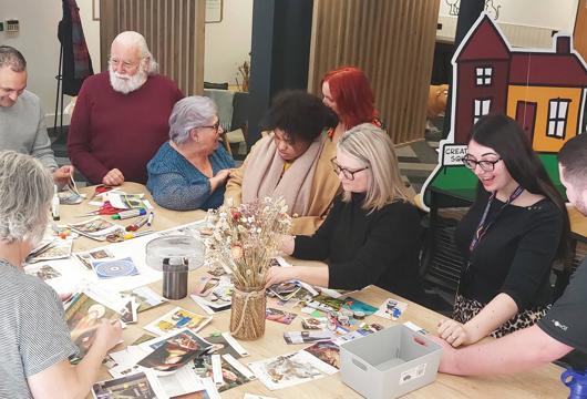 Photo is of a group of customers and colleagues playing game of homes around a table