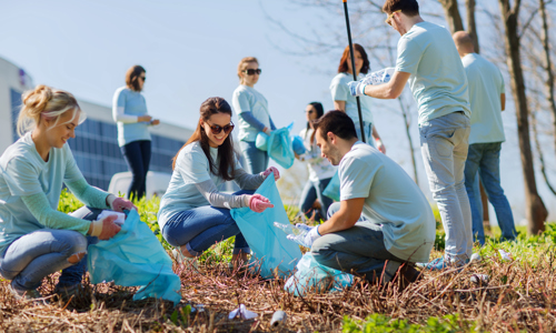 group of happy volunteers with garbage bags cleaning area in park