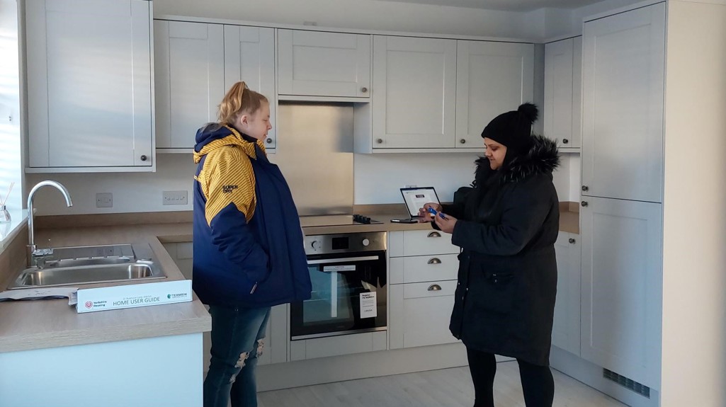 A photograph of customer Faye moving into her new home, standing in her new kitchen.