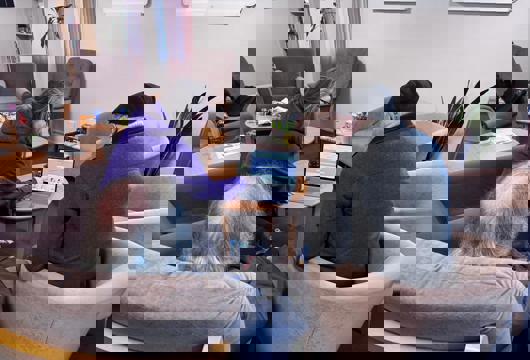 A Yorkshire Housing colleagues sits at a table showing the National Support Network on a laptop to two customers seated in armchairs in a quiet lounge area with coffee tables and plants.