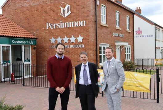 Three people stood outside a Persimmon show home smiling at the camera. 