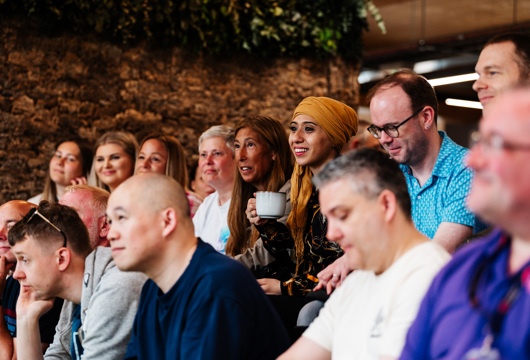 A group of people sat smiling together and someone giving a presentation 