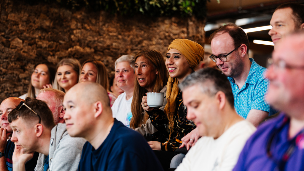 A group of people sat smiling together and someone giving a presentation 