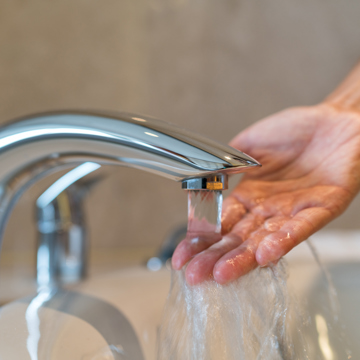 Tap running with a hand testing the temperature of the water