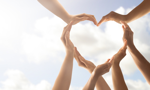 Picture of seven hands together forming the shape of a heart against a sky background