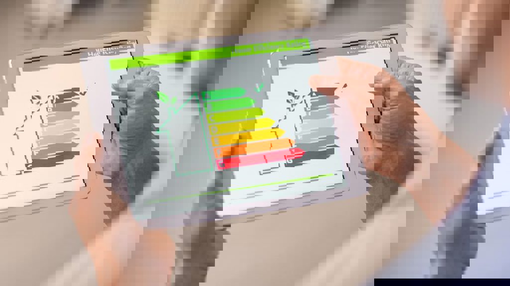 Photograph of hands holding a white iPad-style tablet showing EPC ratings with a tick next to the A rating section.