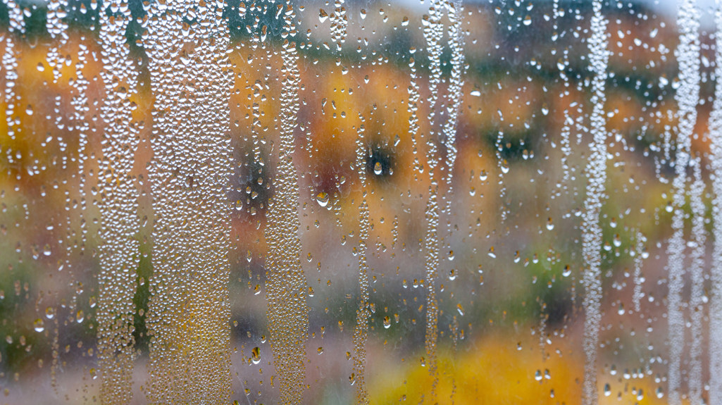 A photo of a blurred view out of a window with condensation running down the window. 