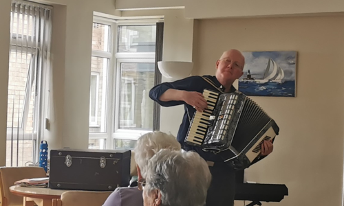 A customer called Roger playing the accordion to two women in a community centre.