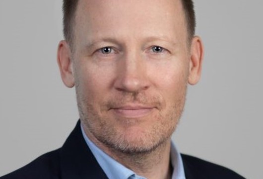 A headshot photo of Dr Rob Archer wearing a navy jacket and light blue shirt.