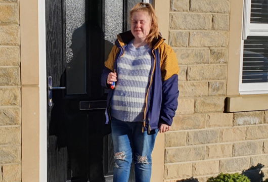 A photograph of customer Faye moving into her new home, standing outside her front door. 