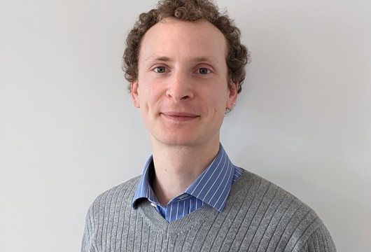 Head-and-shoulders portrait of Dr Guy Marshall wearing a grey jumper and blue striped shirt.