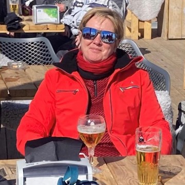 Woman in casual outdoor clothing and sunglasses smiling at camera