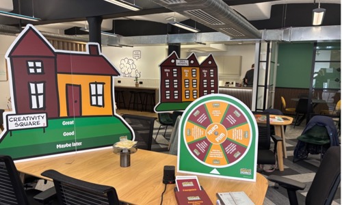 Photo of game of homes set up - there are some big cardboard cut outs, a house, a few tall flats and then a spinning wheel on a table!