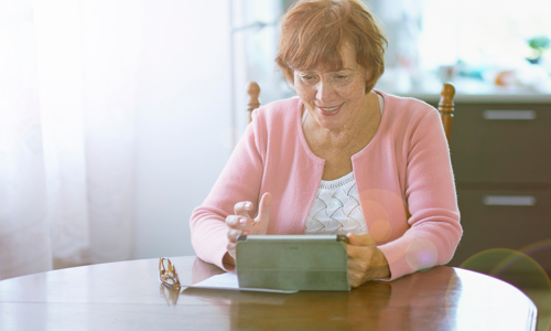 Woman sat at a table on an iPad wearing a pink cardigan