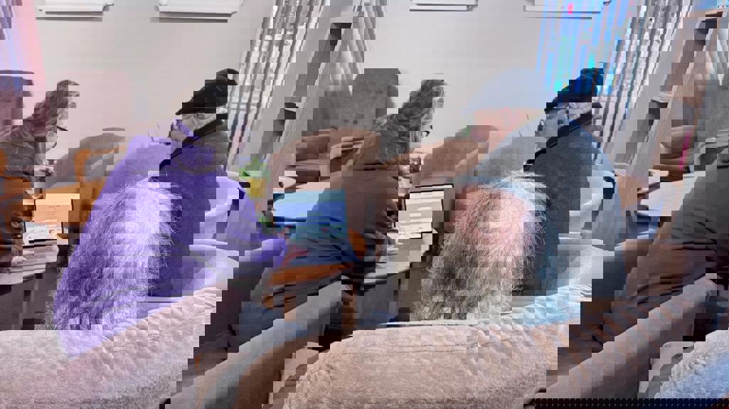 A Yorkshire Housing colleagues sits at a table showing the National Support Network on a laptop to two customers seated in armchairs in a quiet lounge area with coffee tables and plants.