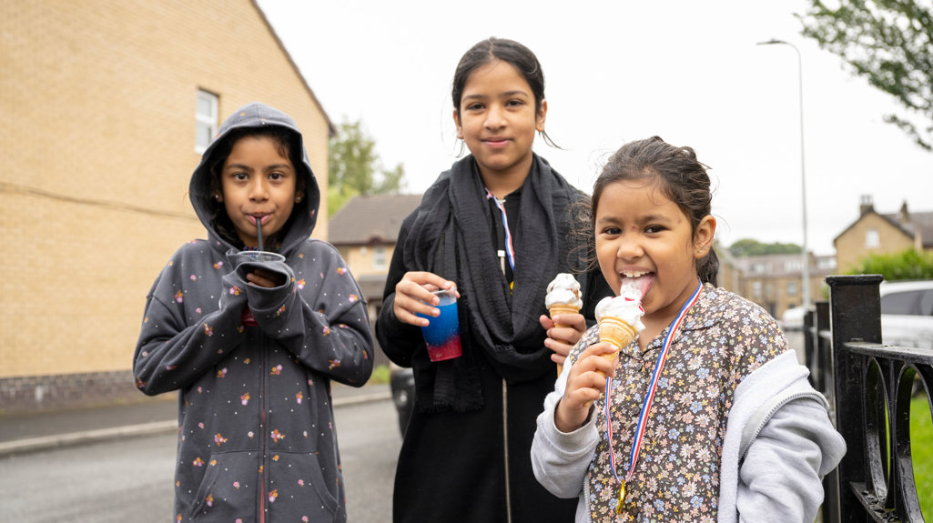 Three children with ice cream standing on the street