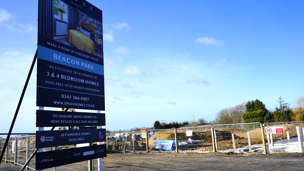 Sign for the Beacon Park housing development next to a fenced construction site under a blue sky.